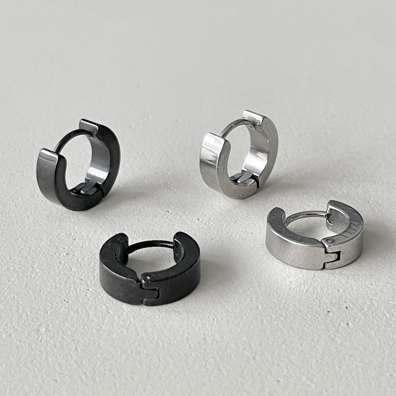 Pu&ograve; includere: Quattro piccoli orecchini a cerchio. Due sono neri e due argentati. Gli orecchini hanno un design semplice e minimalista, con chiusura a cerniera. Gli orecchini sono in metallo. Diametro di circa 1,5 cm.