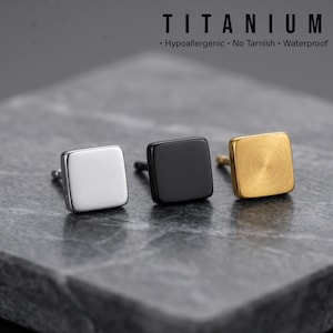 May include: Three square stud earrings in silver, black, and gold. The earrings are displayed on a grey surface. The word "TITANIUM" is at the top of the image, with the words "Hypoallergenic, No Tarnish, Waterproof" below.