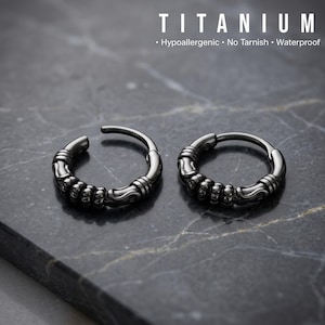 May include: Two silver-colored titanium hoop earrings with a textured design. The earrings are on a dark gray marble surface. The word "TITANIUM" is at the top of the image, along with the words "Hypoallergenic, No Tarnish, Waterproof."