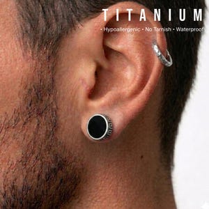 K&ouml;nnte beinhalten: Ein schwarzer und silberner Titan-Ohrstecker mit einem griechischen Schl&uuml;sseldesign am Rand. Das Bild zeigt auch einen silbernen Creolen-Ohrring und das Wort "TITANIUM" oben, mit dem Text "Hypoallergen &bull; Kein Anlaufen &bull; Wasserdicht".