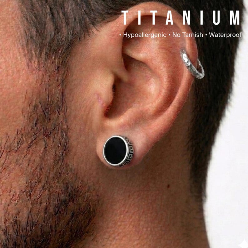 K&ouml;nnte beinhalten: Ein schwarzer und silberner Titan-Ohrstecker mit einem griechischen Schl&uuml;sseldesign am Rand. Das Bild zeigt auch einen silbernen Creolen-Ohrring und das Wort "TITANIUM" oben, mit dem Text "Hypoallergen &bull; Kein Anlaufen &bull; Wasserdicht".