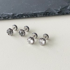 May include: Four silver earrings with a decorative design and a single black or clear stone in the center.