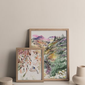 May include: Two framed watercolor paintings, one depicting a landscape with a mountain range and the other featuring a bird flying through a floral design.