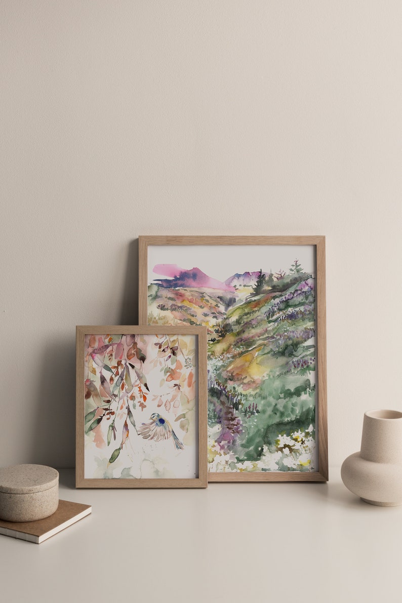May include: Two framed watercolor paintings, one depicting a landscape with a mountain range and the other featuring a bird flying through a floral design.