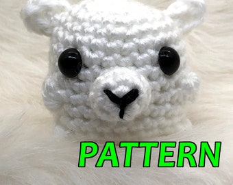 Puede incluir: Cabeza de llama de crochet blanco con ojos negros y nariz negra. La llama está sentada sobre una superficie blanca y esponjosa. El texto "PATTERN" está escrito en letras verdes debajo de la llama.