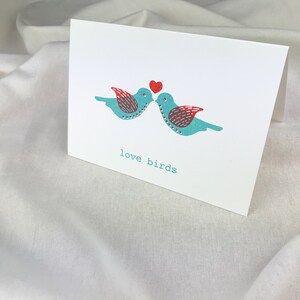 May include: A greeting card with two blue birds kissing with a red heart above them. The text "love birds" is printed below the birds.