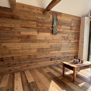 Könnte beinhalten: Ein rechteckiger Couchtisch aus Holz mit vier Beinen und einer glatten Oberfläche, auf dem drei Keramiktassen stehen. Der Tisch befindet sich in einem Raum mit horizontaler Holzpaneelwand und einem passenden Holzdielenboden.