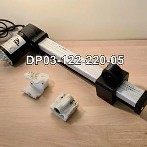 May include: An electric linear actuator with a black motor and a silver and black body. Two white plastic mounting brackets are also present. The text "DP03-122-220-05" is printed on the image.