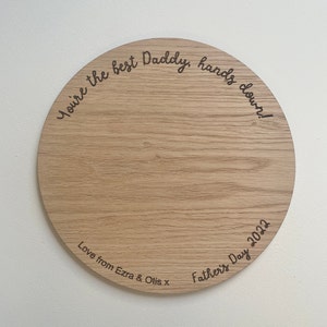 May include: A round wooden plaque with the text "You're the best Daddy, hands down!" and "Love from Ezra & Otis x Father's Day 2022" engraved on it.