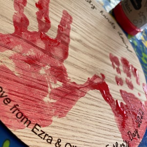 May include: A wooden plaque with red handprints and the text "You're the best Daddy hands down Love from Ezra & Otis x Father's Day 2022".