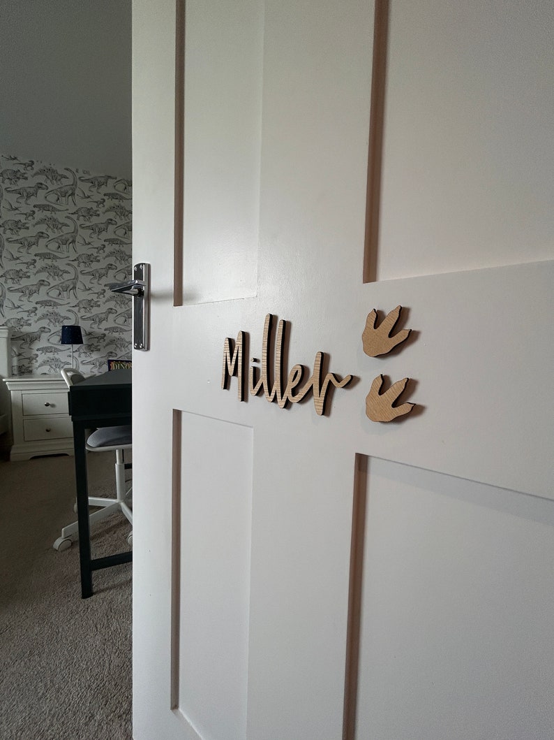 May include: A white door with a wooden name sign that says "Miller" with two dinosaur footprints on the right side of the sign.