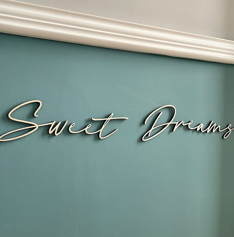 May include: White wooden sign with the words "Sweet Dreams" written in a cursive font against a light blue wall.