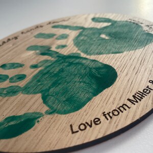 May include: A round wooden plaque with two green handprints and the text "World's Best Daddy Hands Down Love from Miller & Olive X"