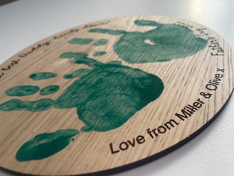 May include: A round wooden plaque with two green handprints and the text "World's Best Daddy Hands Down Love from Miller & Olive X"