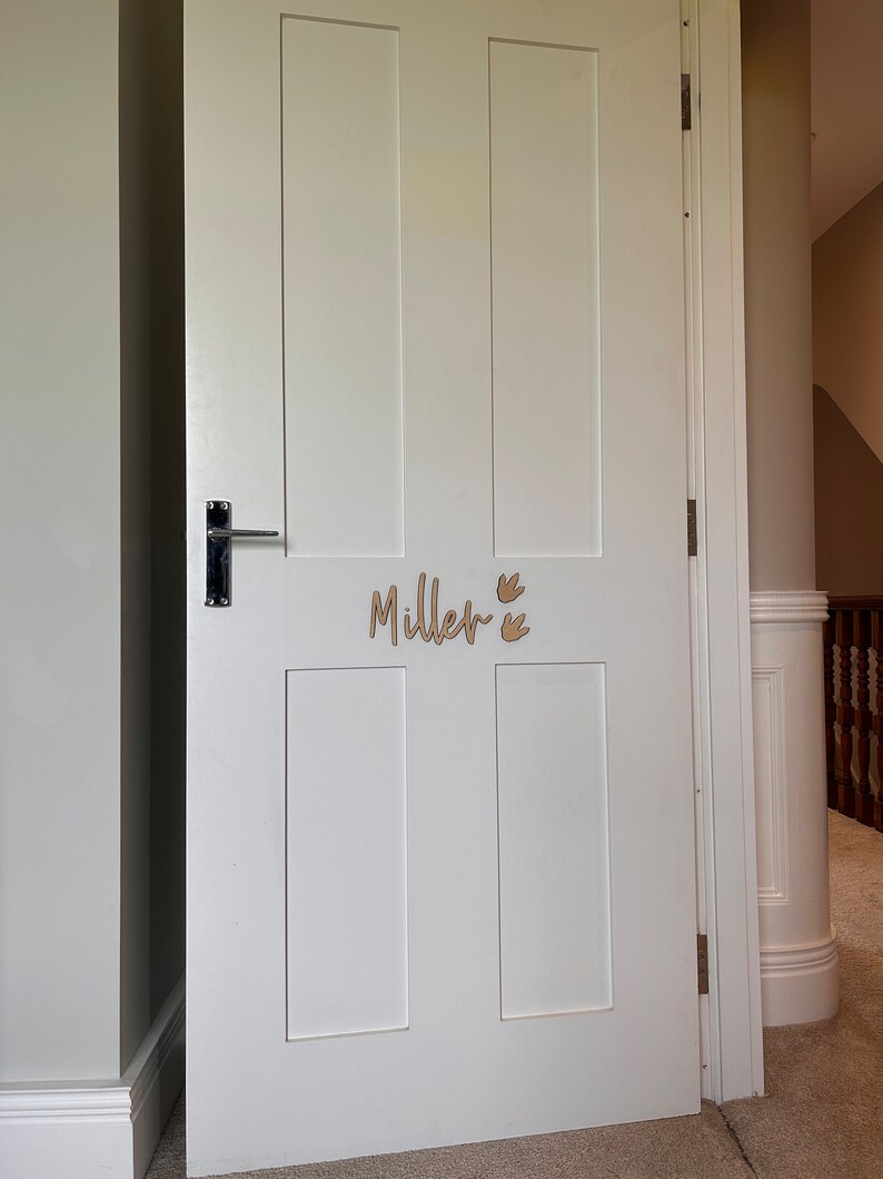 May include: White interior door with a wooden name sign that reads "Miller" with two small bird cutouts above the name.