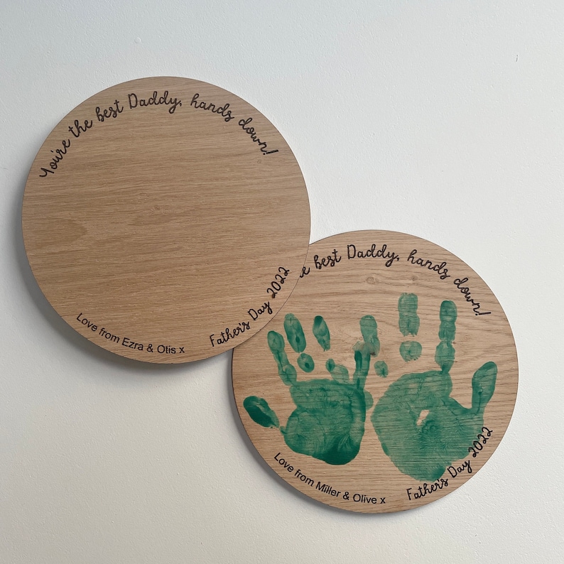 May include: Two round wooden plaques with handprint art and the text "You're the best Daddy, hands down!" and "Love from Ezra & Otis X" on one plaque and "Love from Miller & Olive x" on the other plaque.