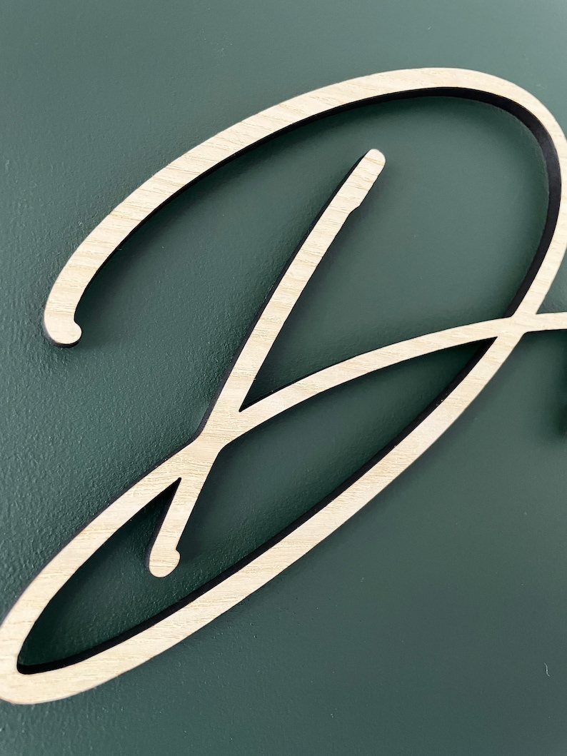 May include: A close-up of a wooden letter D, painted in a light wood color, with a dark brown outline. The letter is on a dark green background.