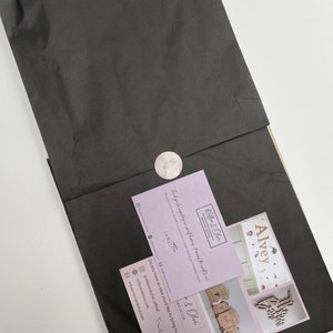 May include: A pink and white business card with the text "Miller & Olive Bespoke Decor" and the text "Thank you for supporting my small business!"  The card also includes a website address, Instagram handle, and email address. The card is sitting on top of a black piece of tissue paper.