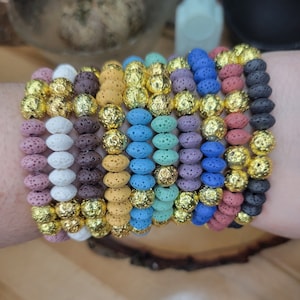 May include: A set of 12 bracelets made of lava rock beads with gold accents. The bracelets are in various colors, including white, brown, yellow, blue, purple, and red.