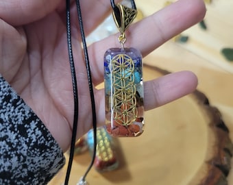 May include: A gold-toned pendant necklace with a clear resin charm featuring a multi-colored stone arrangement and a gold geometric design. The necklace is on a black cord.