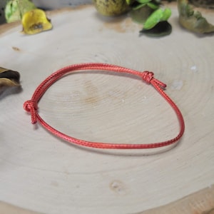 May include: A simple red string bracelet with a knot on one end.