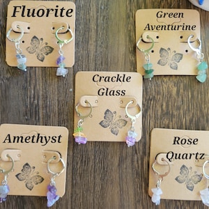 May include: Six pairs of earrings with different gemstone charms. The charms are labeled "Fluorite", "Green Aventurine", "Crackle Glass", "Amethyst", "Rose Quartz".