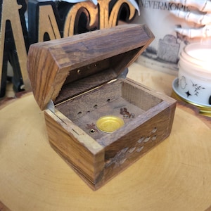 May include: A white ceramic mug with a black handle and the text "But First, Coffee" in a bold, black font. The mug is set against a blurred background, suggesting a cozy setting.