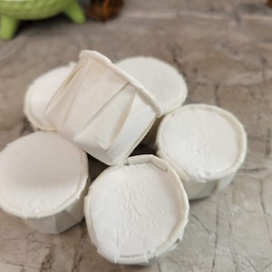 May include: A close-up of six white paper cupcake liners stacked on top of each other. The liners are made of a thin, white paper and have a fluted edge.