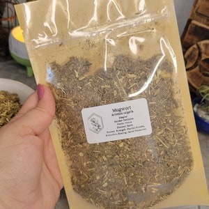 May include: A clear plastic bag filled with dried mugwort, a type of herb used in herbalism and magic. The bag has a label that reads "Mugwort, Artimisia vulgaris, Magical, Gender: Feminine, Planet: Venus, Element: Earth, Powers: Strength, Psychic Powers, Protection, Healing, Astral Projection."