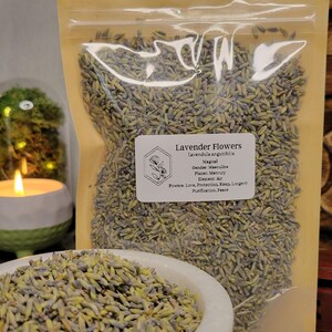 May include: A clear plastic bag filled with dried lavender flowers. The bag has a label that reads "Lavender Flowers, Lavendula angutifolia, Magical, Gender: Masculine, Planet: Mercury, Element: Air, Powers: Love, Protection, Sleep, Longevity, Purification, Peace."
