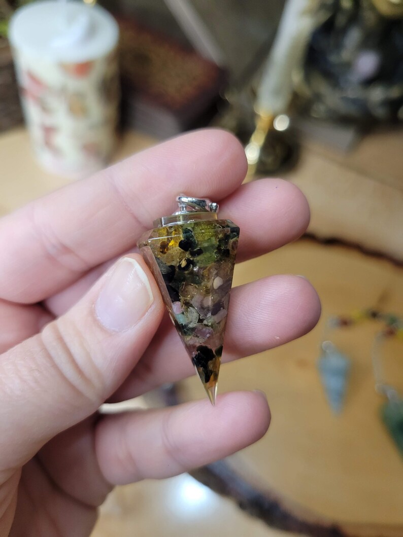 May include: A clear crystal pyramid pendant with a silver bail. The pyramid is filled with various small crystals, including green, brown, pink, and black.