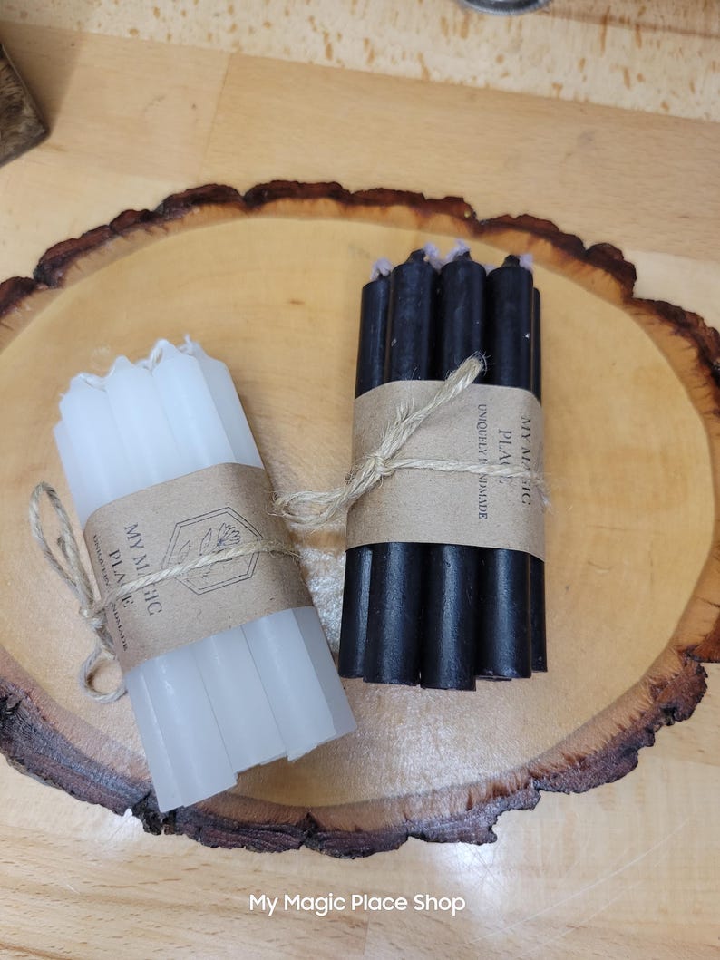 May include: Two bundles of thin, cylindrical candles, one white and one black, each wrapped in a brown paper band tied with twine. The paper bands feature the text My Magic Place and Uniquely Handmade. The candles are arranged in small groups.