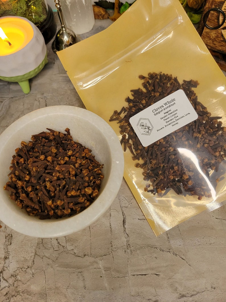 Puede incluir: Un primer plano de una bolsa de clavos enteros, una especia popular utilizada en la cocina y por sus propiedades medicinales. La bolsa est&aacute; etiquetada como "Clavos enteros" y enumera el nombre bot&aacute;nico "Syzygium aromaticum". La etiqueta tambi&eacute;n menciona los usos m&aacute;gicos de los clavos, incluida la protecci&oacute;n, el exorcismo, el amor y el dinero.