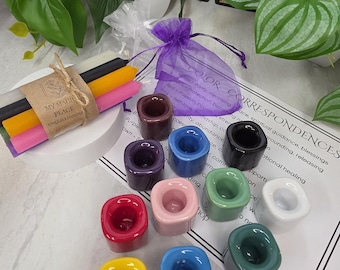 May include: A set of ten small, square-shaped ceramic candle holders in various colors including yellow, blue, green, white, pink, red, purple, brown, and black, alongside a bundle of four taper candles wrapped in a brown paper label.