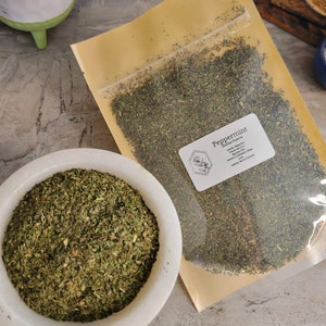 May include: A close-up of a bag of dried peppermint leaves. The bag is labeled "Peppermint Mentha Piperita" and lists the ingredients as "Organic Peppermint Leaves".