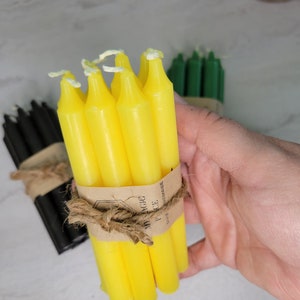 May include: A bundle of bright yellow taper candles secured with a brown paper band and tied with natural jute twine. The paper band features the text MY MAGIC PIECE and UNIQ HANDMADE. Additional bundles of black and green candles are visible nearby.