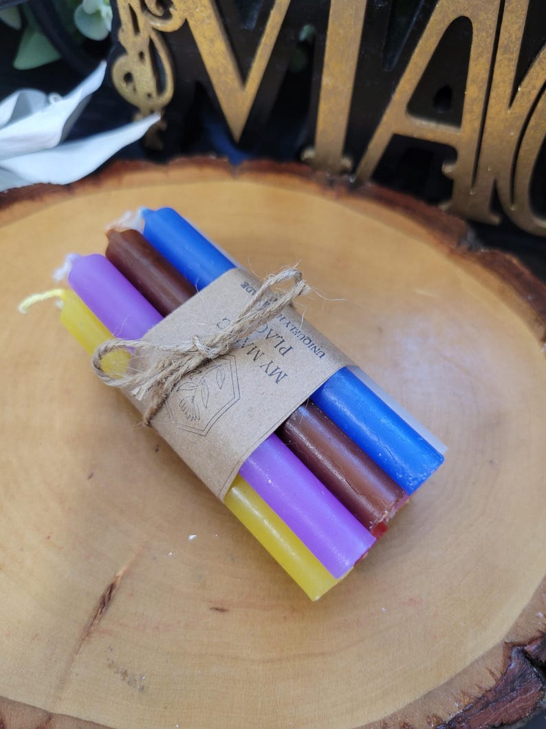 May include: A bundle of four thin taper candles in yellow, purple, brown, and blue, tied together with a piece of twine. A brown paper label is wrapped around the center, featuring a line drawing of a flower and the text MY MADE PLACE.