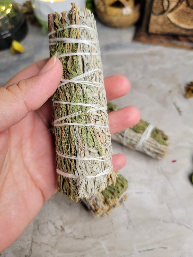 Pu&ograve; includere: Un mazzo di bastoncini di salvia e cedro legati insieme con uno spago. I bastoncini di salvia sono di colore verde chiaro e grigio.