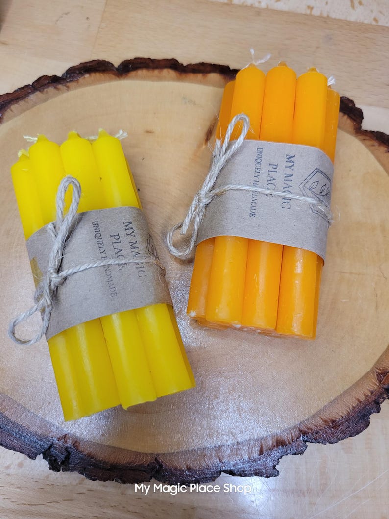 May include: Two bundles of thin taper candles, one set in bright yellow and one in deep orange. Each bundle is wrapped in a brown paper band labeled My Magic Place Uniquely Handmade and tied with a thin jute string, resting on a round wood slice.