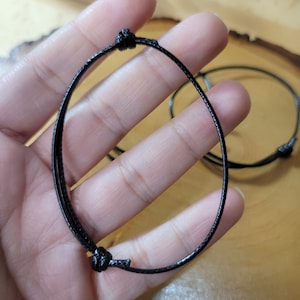 May include: Two black adjustable cord bracelets with a simple knot closure.
