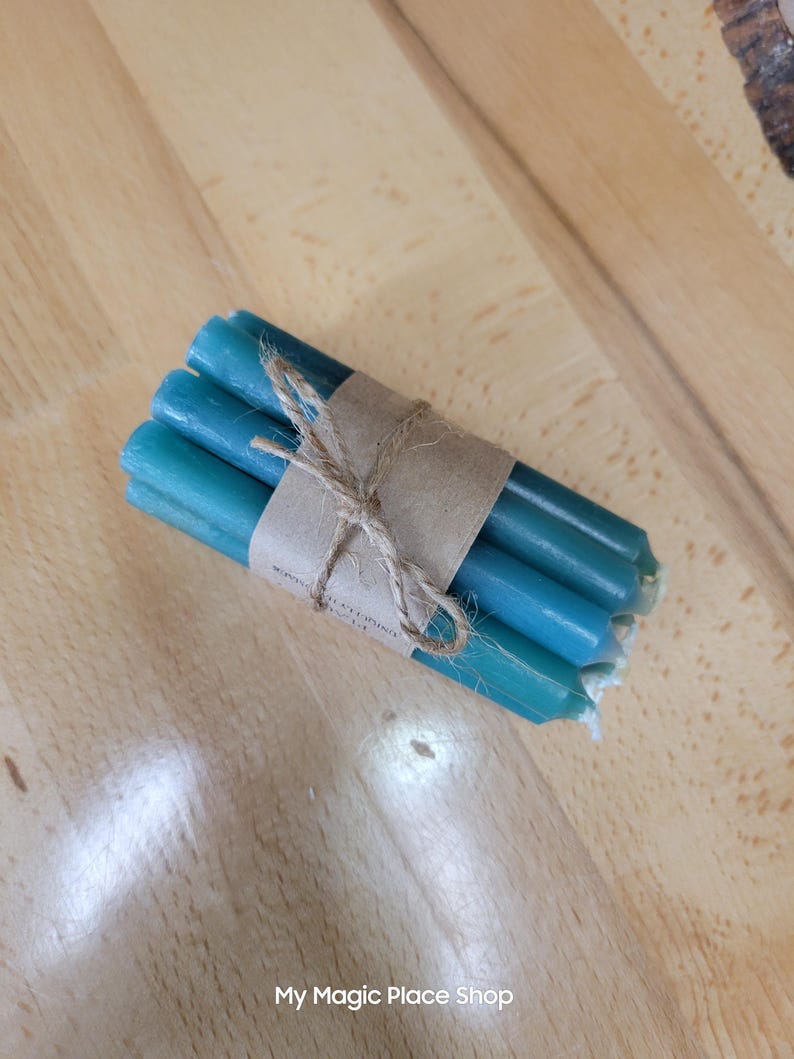 May include: A bundle of five slender teal-colored taper candles secured with a brown paper band and tied with a thin jute twine string. The candles are cylindrical with flat ends and are arranged in a compact group. The text My Magic Place Shop is visible.