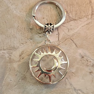 May include: Silver key chain with a clear crystal sun and moon charm. The charm has a silver sun with a crescent moon inside.