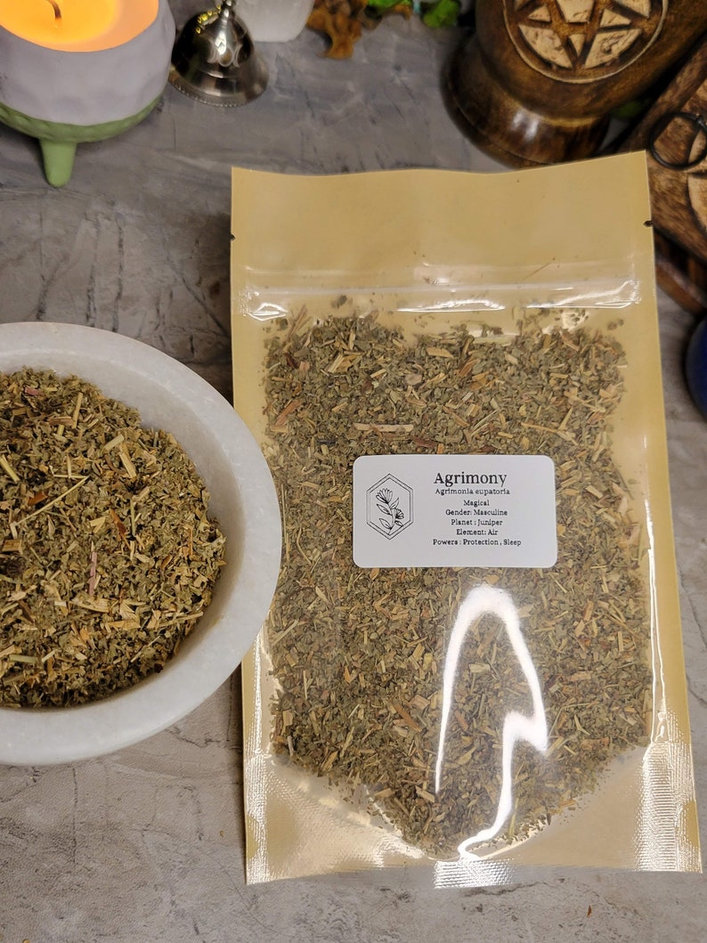 May include: A close-up of a bag of dried Agrimony herb. The bag is labeled with the name of the herb, its magical properties, and its planetary association. The label reads: "Agrimony, Agrimonia eupatoria, Magical, Gender: Masculine, Planet: Juniper, Element: Air, Powers: Protection, Sleep."