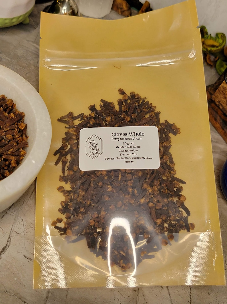 Puede incluir: Un primer plano de una peque&ntilde;a bolsa de pl&aacute;stico transparente llena de clavos de olor enteros. La bolsa est&aacute; etiquetada como "Clavos de olor enteros Syzygium aromaticum" y enumera las propiedades m&aacute;gicas de los clavos de olor, incluida la protecci&oacute;n, el exorcismo, el amor y el dinero.