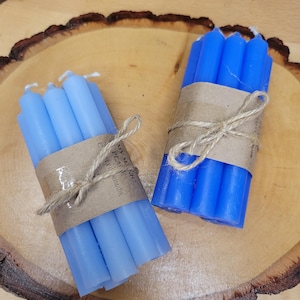 May include: Two bundles of thin taper candles, one light blue and one vibrant blue, each wrapped in a brown paper band tied with natural twine. The paper bands feature the printed text My Magic Place Shop and the words handmade.