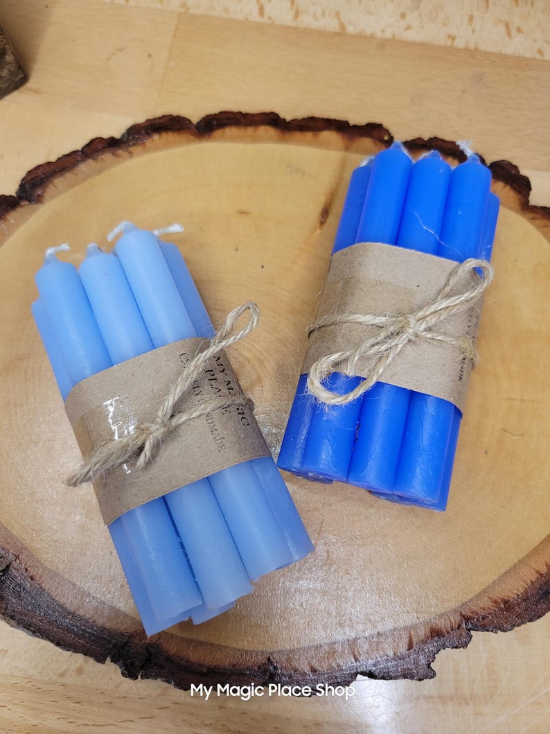 May include: Two bundles of thin taper candles, one light blue and one vibrant blue, each wrapped in a brown paper band tied with natural twine. The paper bands feature the printed text My Magic Place Shop and the words handmade.