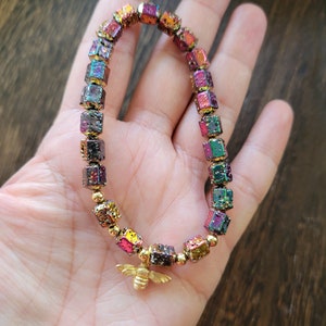 May include: A multi-colored iridescent bracelet with gold cube beads and a gold bee charm.