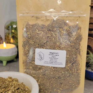 May include: A resealable brown pouch filled with dried mugwort herb. The pouch has a label that reads "Mugwort Artimisia vulgaris Magical Gender: Feminine Planet: Venus Element Earth Powers: Strength, Psychic Powers, Protection, Healing, Astral Projection"