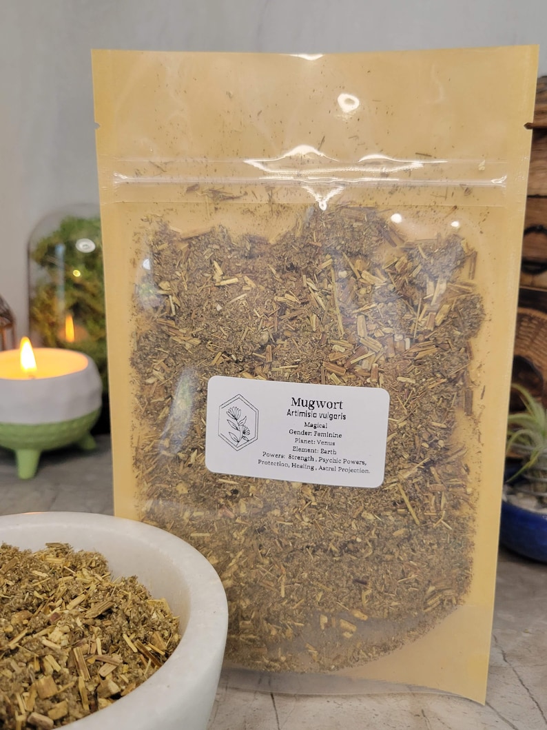 May include: A resealable brown pouch filled with dried mugwort herb. The pouch has a label that reads "Mugwort Artimisia vulgaris Magical Gender: Feminine Planet: Venus Element Earth Powers: Strength, Psychic Powers, Protection, Healing, Astral Projection"