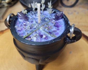 May include: A black cauldron-shaped candle with a purple wax interior. The candle is decorated with amethyst crystals, dried lavender, and a central wick. The cauldron has three small legs and two metal handles.